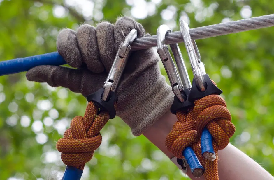 Close-up of a climber's gloved hand securing carabiners on a cable, showcasing outdoor activity gear.